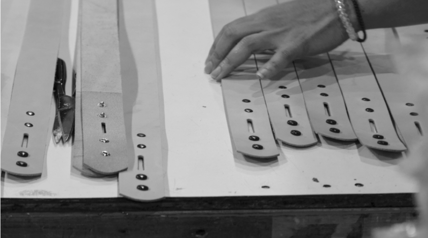 Hands arranging cut leather belt straps on a workbench