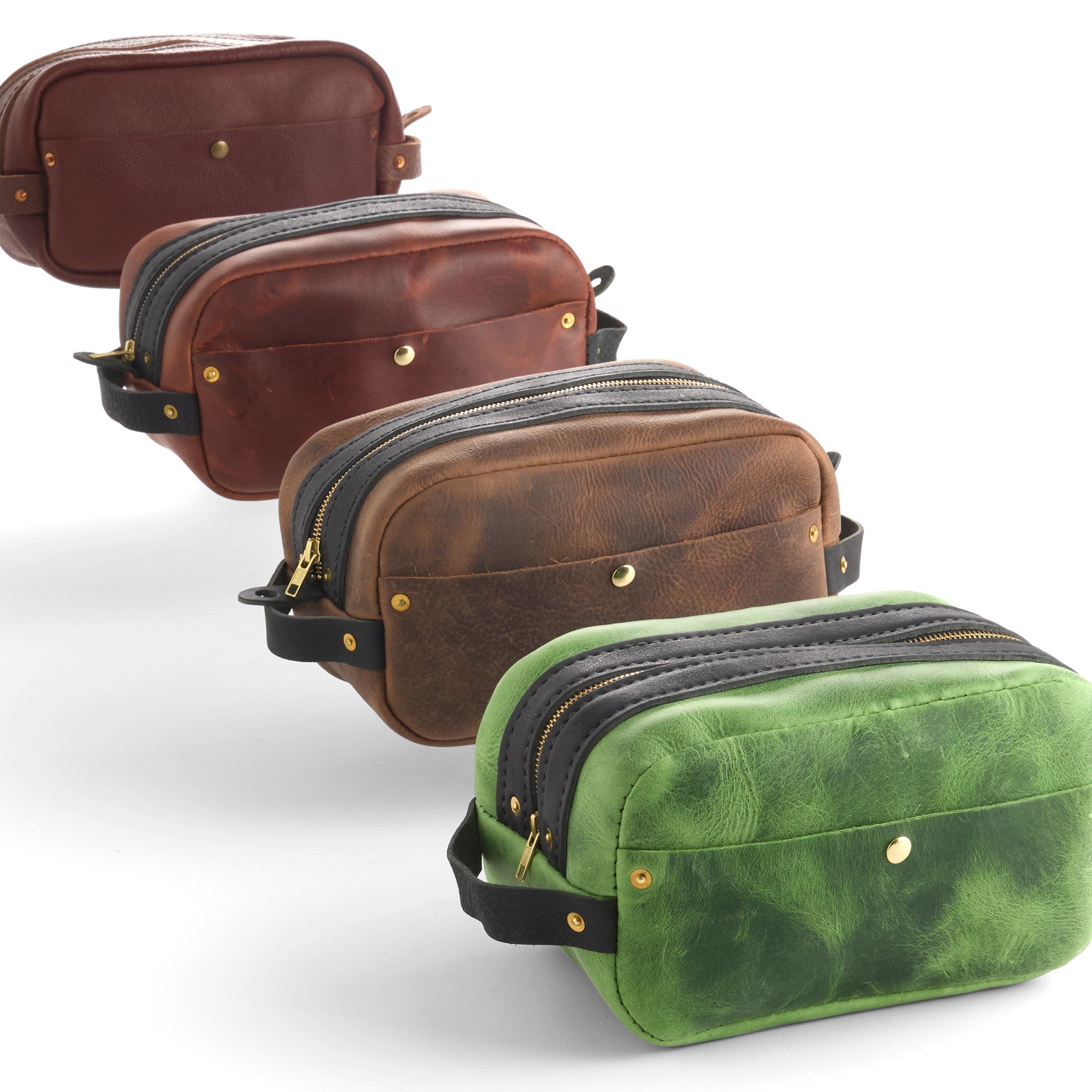 Four leather zip pouches in brown and green tones arranged diagonally on a white background, each with a black zipper, gold-tone hardware, and a small strap.